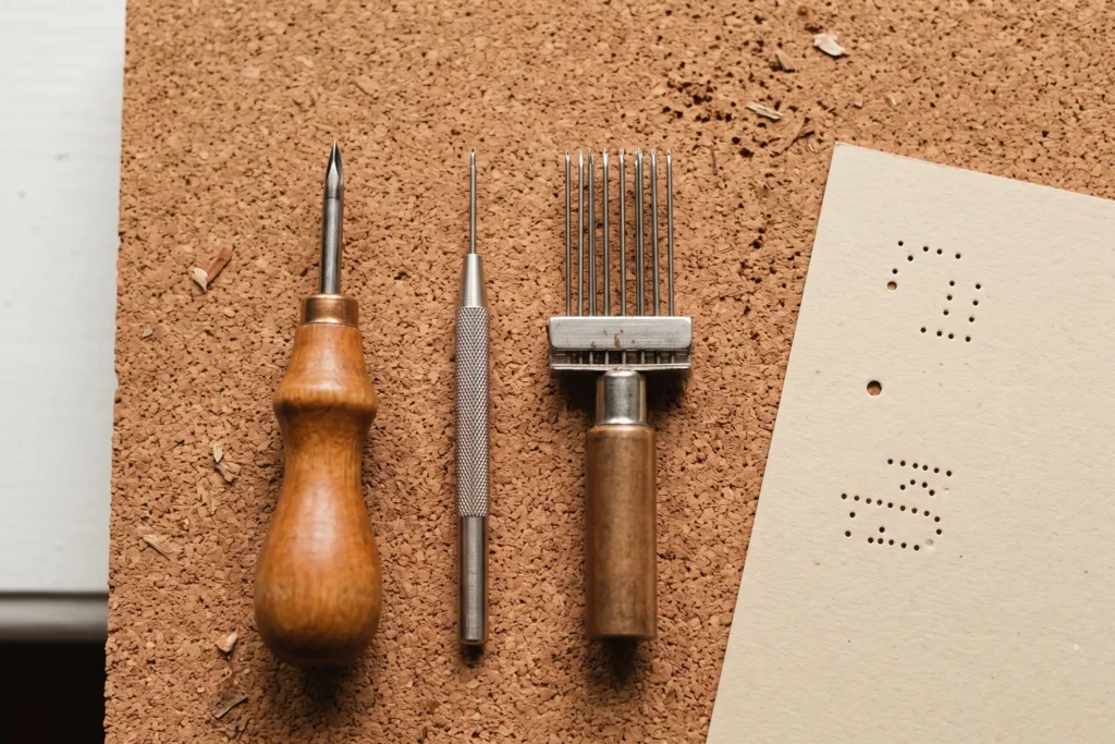 Distintos punzones para papel sobre una mesa: de mango de madera, de punta fina y una herramienta de varias agujas